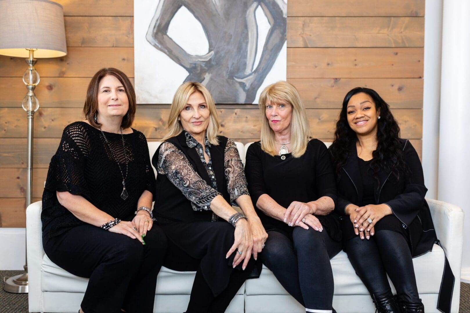 Four women sitting on a couch in front of a painting.