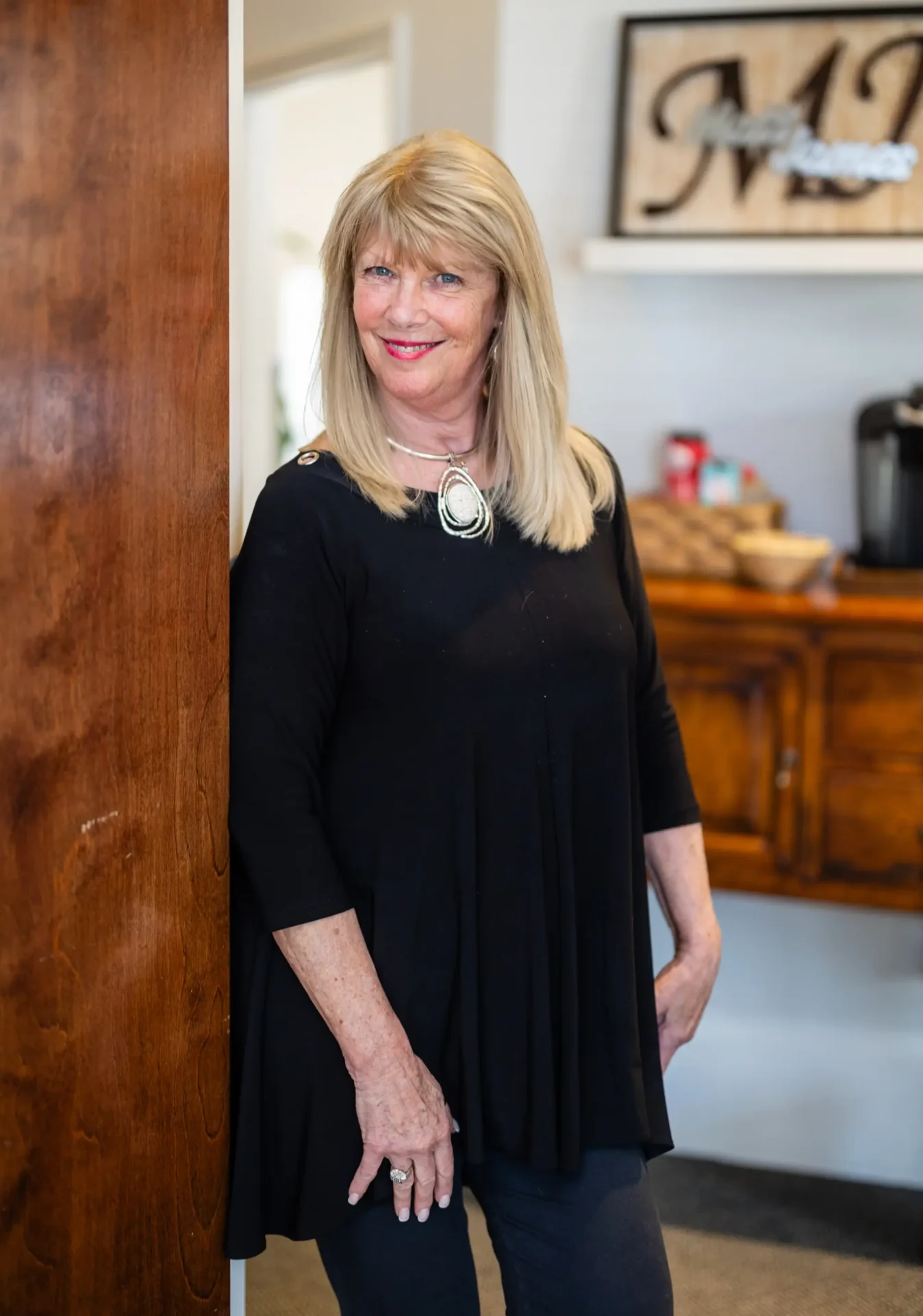 A woman in black dress standing next to wooden door.